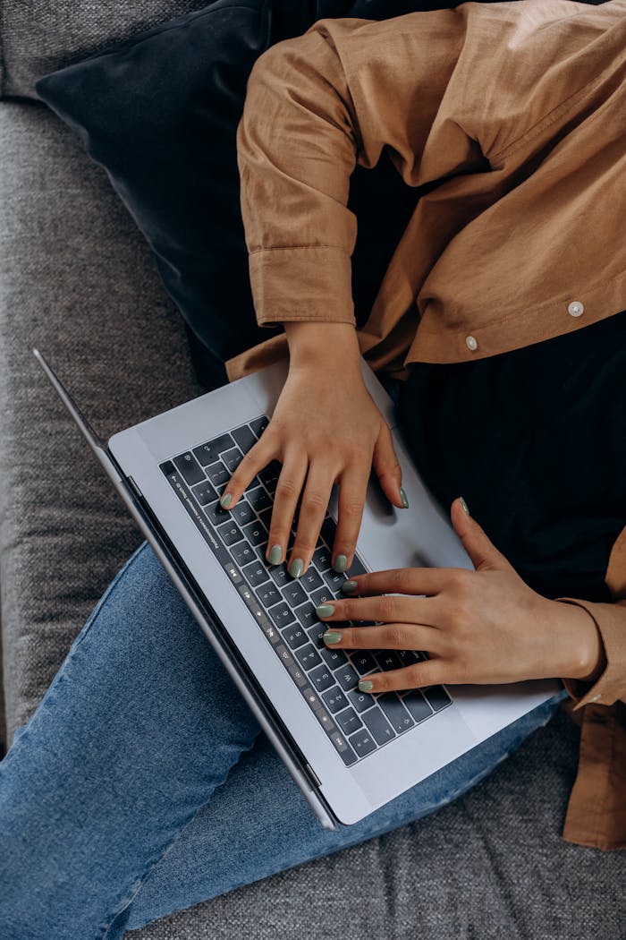 services-01 A person typing on a laptop while seated on a couch with casual attire, perfect for remote work imagery.